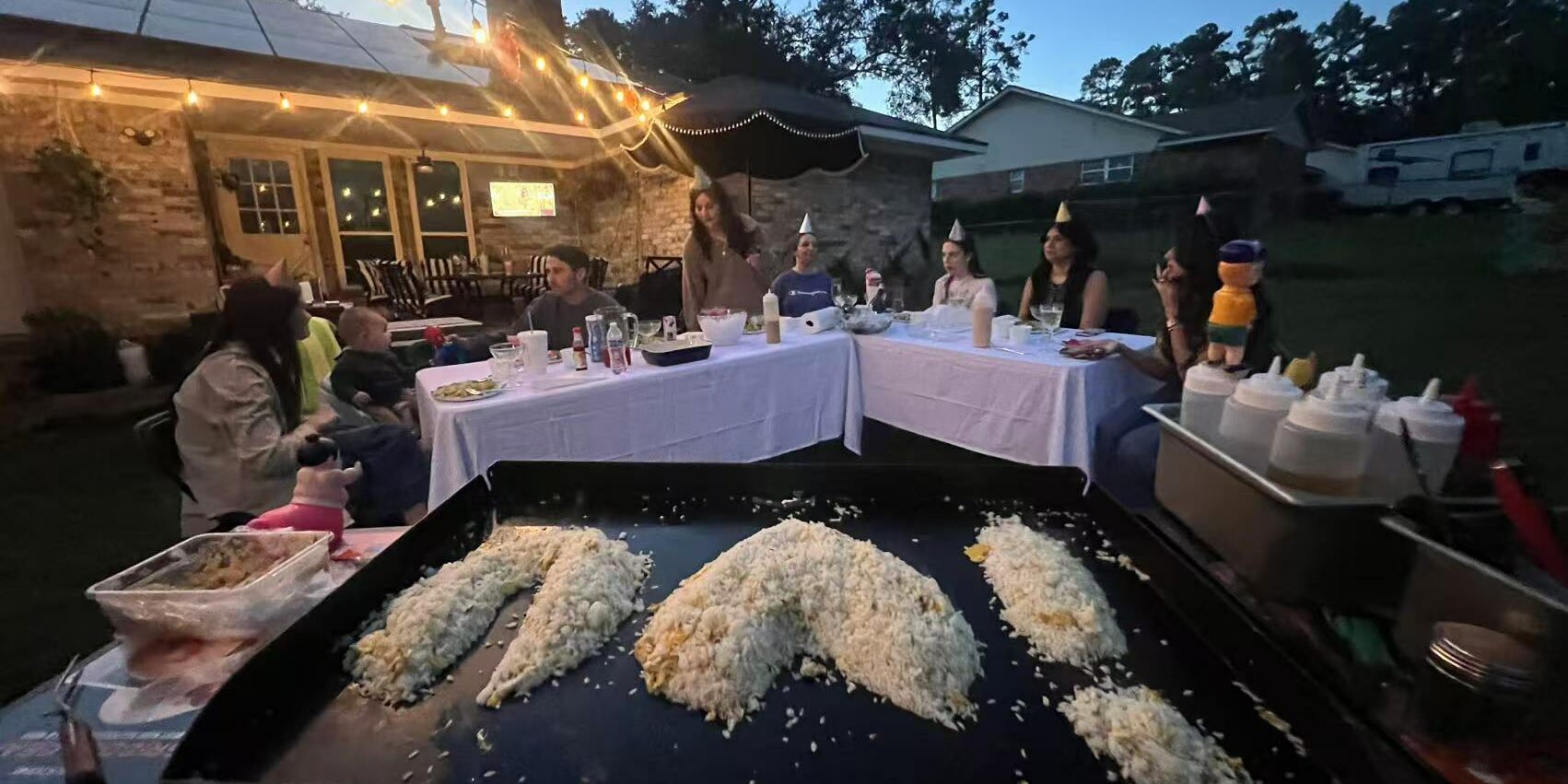 Family hibachi at home dinner with a child and adults seated around the grill during an evening backyard gathering