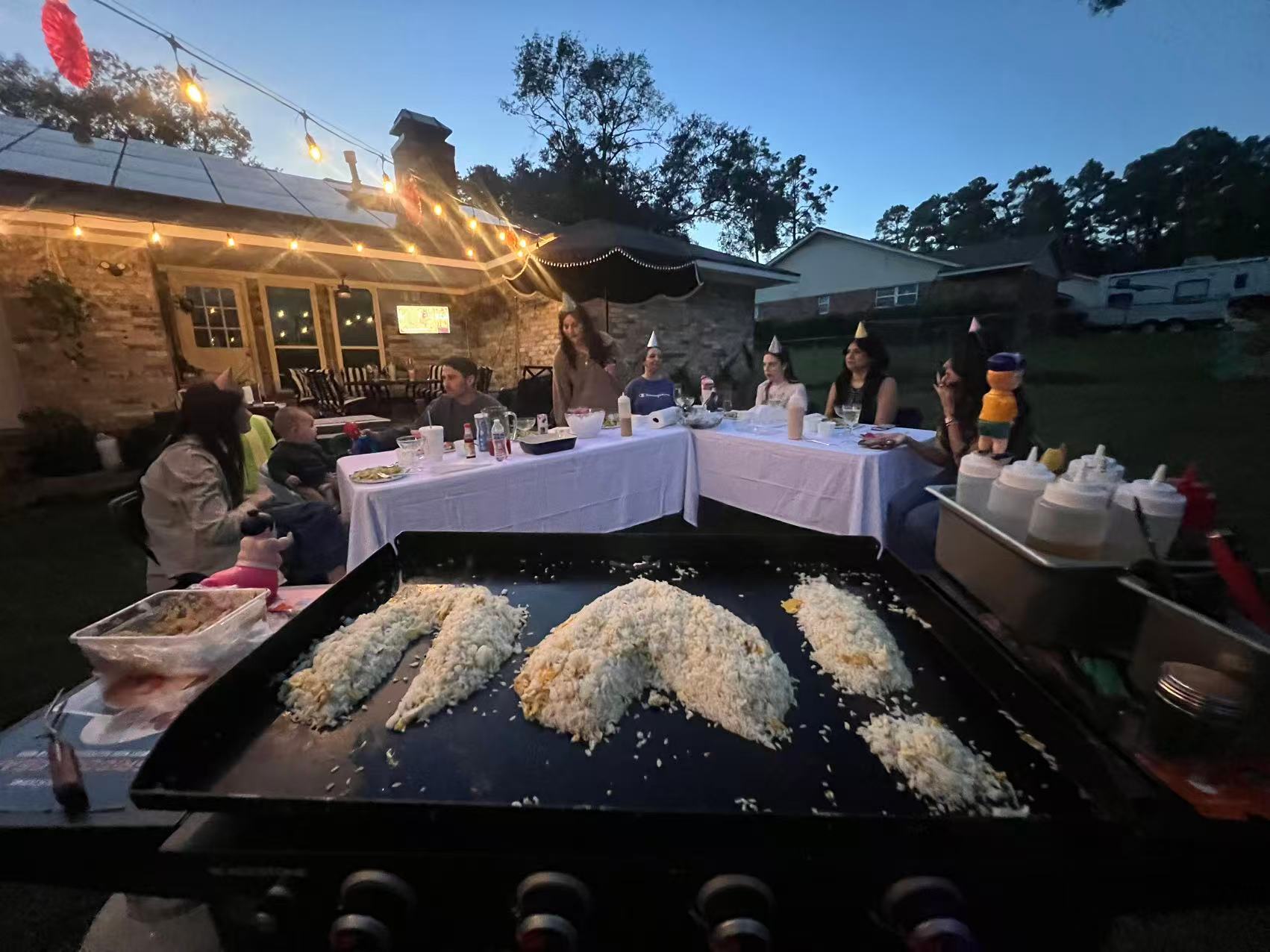 Family hibachi at home dinner with a child and adults seated around the grill during an evening backyard gathering