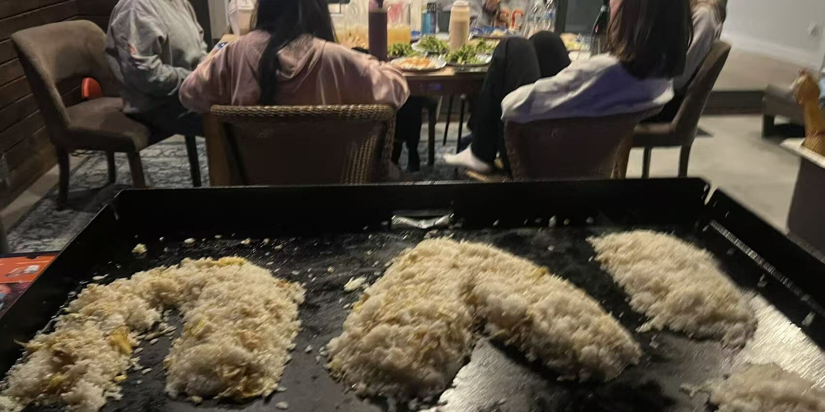Family seated around an at-home hibachi grill with clear spacing for a private dinner party