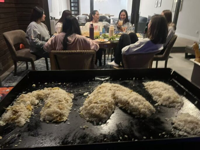 Family seated around an at-home hibachi grill with clear spacing for a private dinner party