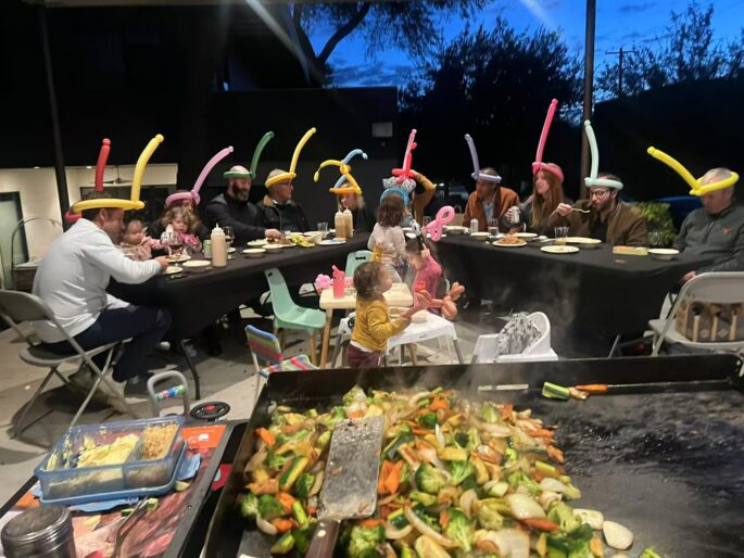 Hibachi at home allergy questions checklist for a backyard dinner with vegetables cooking on the grill and guests seated nearby