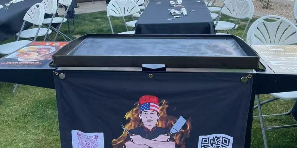 Hibachi 2 Home branded portable grill set up on a backyard lawn beside long guest tables for an evening hibachi party at home