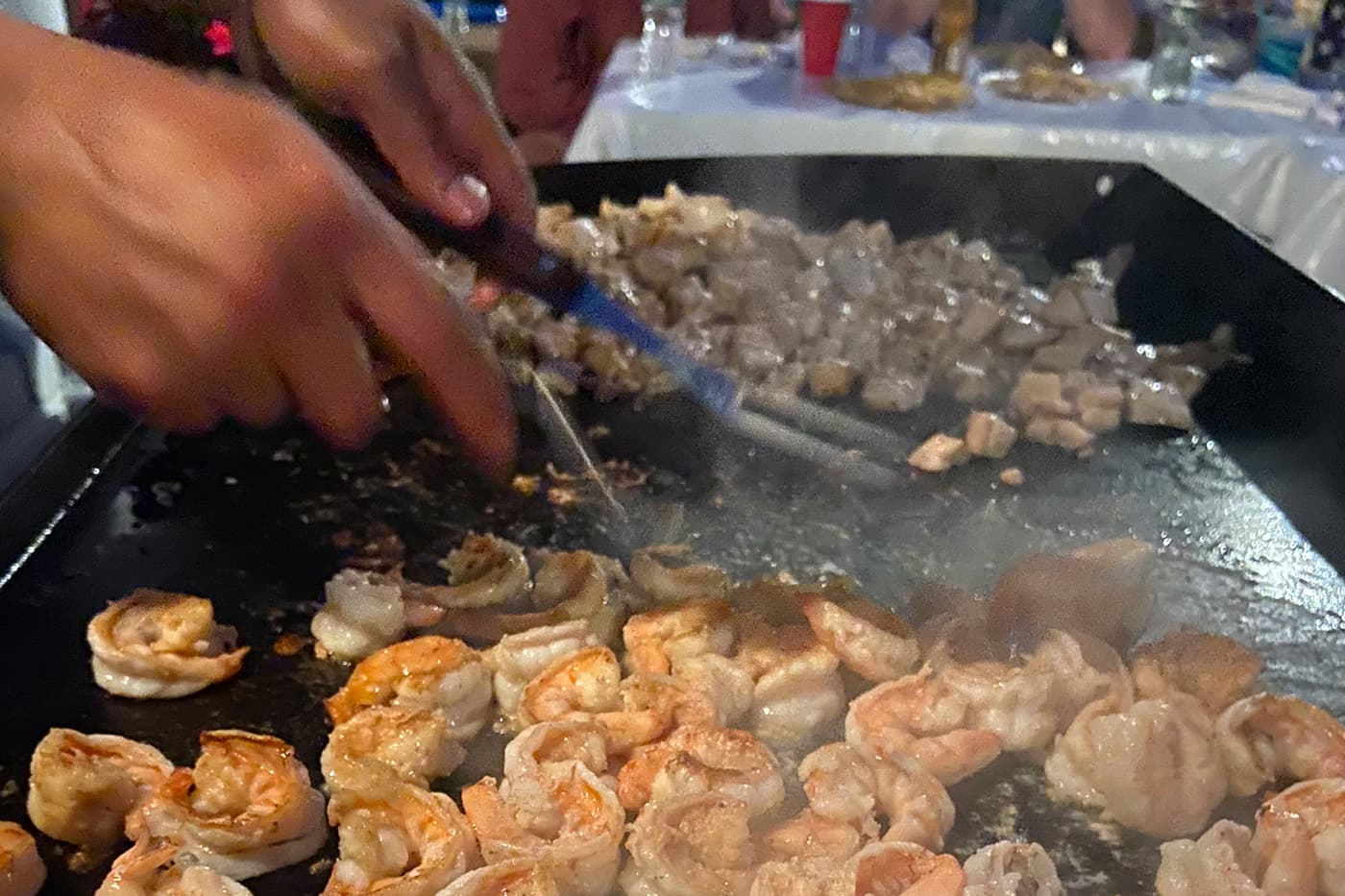 Hibachi chef searing shrimp and diced chicken on a flat-top grill during a private hibachi dinner at home