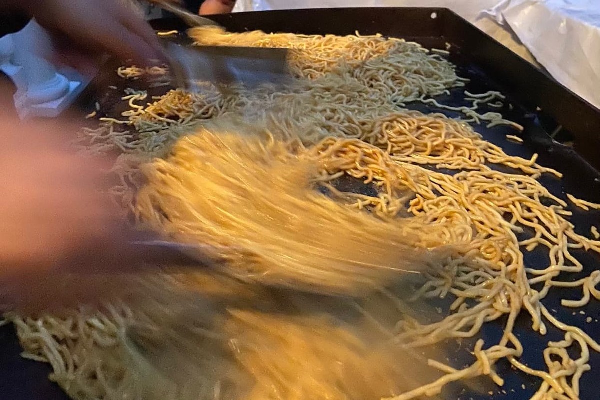 Chef tossing hibachi noodles on a flat-top grill during a private hibachi dinner at home