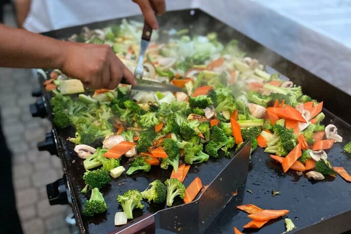 Hibachi chef tossing broccoli, carrots, mushrooms and zucchini on a flat-top grill during a private hibachi dinner